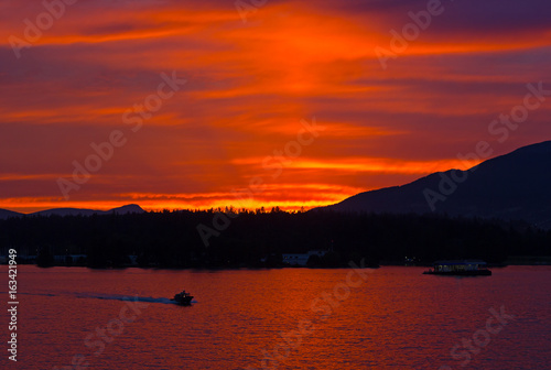 Scarlet sunset over the city of Vancouver, BC, Canada. Mountains landscape during sunset with water and high pine trees on horizon.
