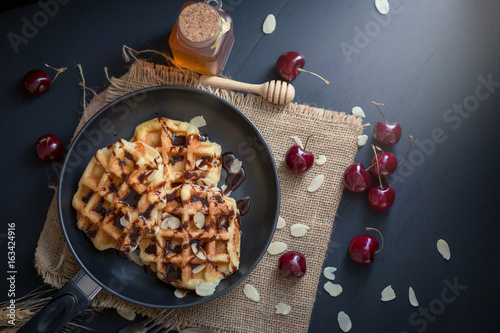 Honey on waffles with cherry berries on dark wooden background. breakfast concept photo