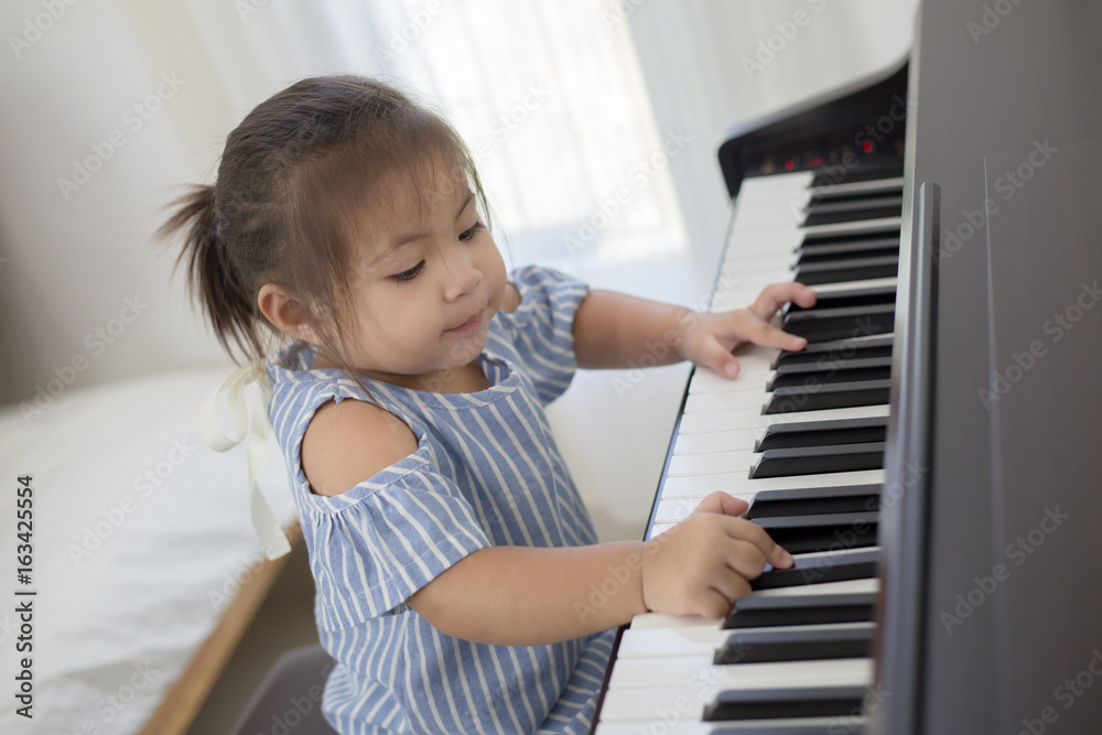 Fototapeta Happy little Asian girl playing piano at home