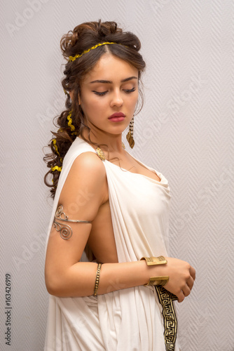 portrait of a beautiful graceful greek young woman in a traditional antique white tunic standing side and looking down