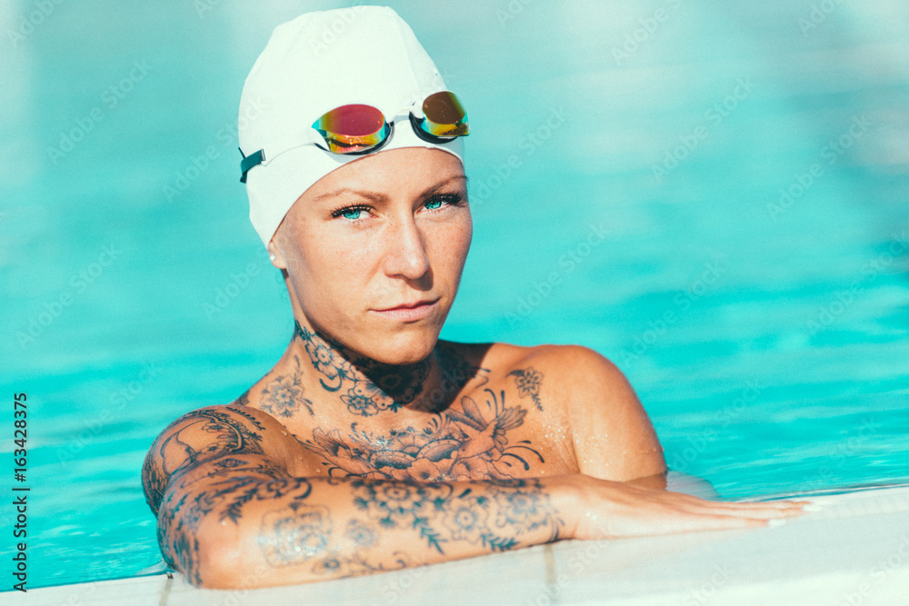 Portrait of female swimmer with tattoos posing by the pool