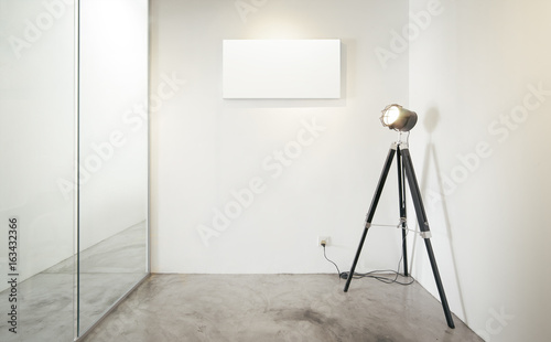 Empty office waiting room, Glass window to the left, Vintage photography stand lamp to the right .Loft interior style , white canvas print on the center white wall. concrete floor .
