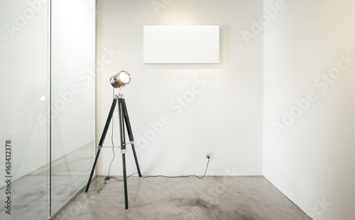 Empty office waiting room, Glass window with vintage photography stand lamp to the left .Loft interior style , white canvas print on the center white wall. concrete floor .