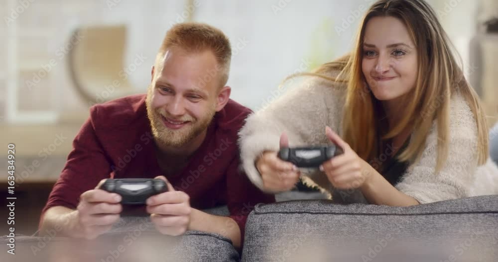 Playful cute couple falling off couch while playing video games Playful cute couple falling off couch while playing video games