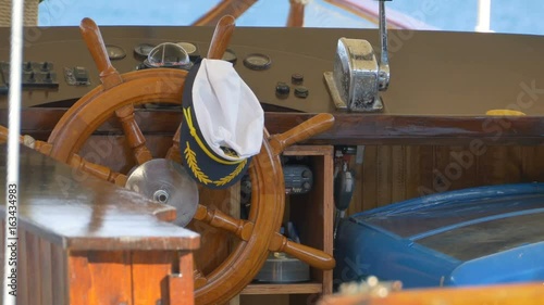 A skipper hat laying on the old steering wheel of a boat.