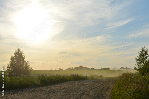 Beautiful summer evening landscape: dust over a rural road and the sun sets, nature, countryside