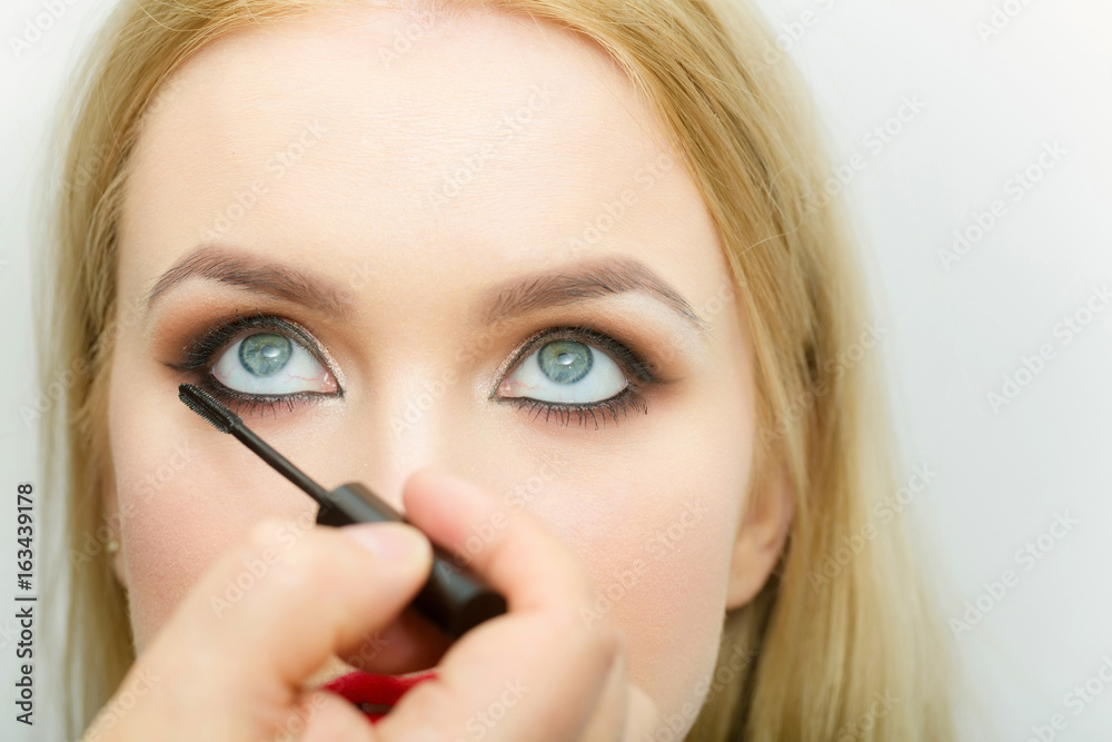 Brush in hand applying black mascara on girl eyelashes