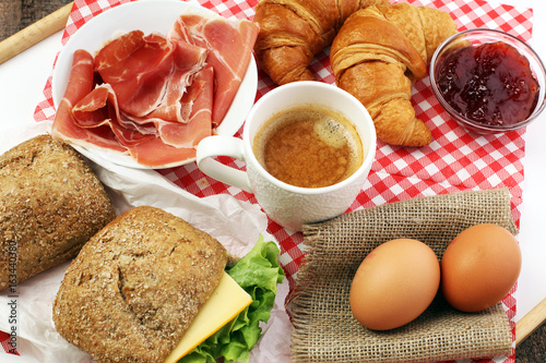 breakfast on table with bread rolls, croissants, coffe and eggs