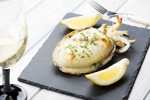 Cuttlefish with garlic and parsley, lemon next to white wine glass on whiteboard. Food.