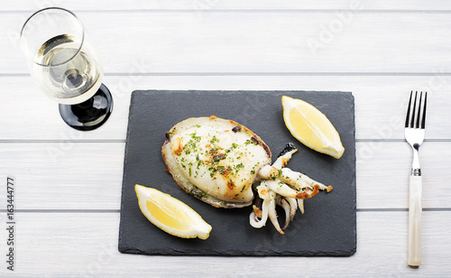 Close-up of cuttlefish with garlic and parsley, lemon next to white wine glass on whiteboard. Food.