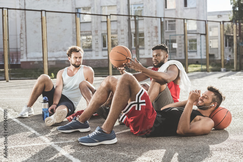 multiethnic group of men resting after basketball game on court