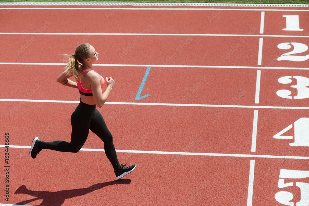 Young sport woman sprinter athlete running on stadium track