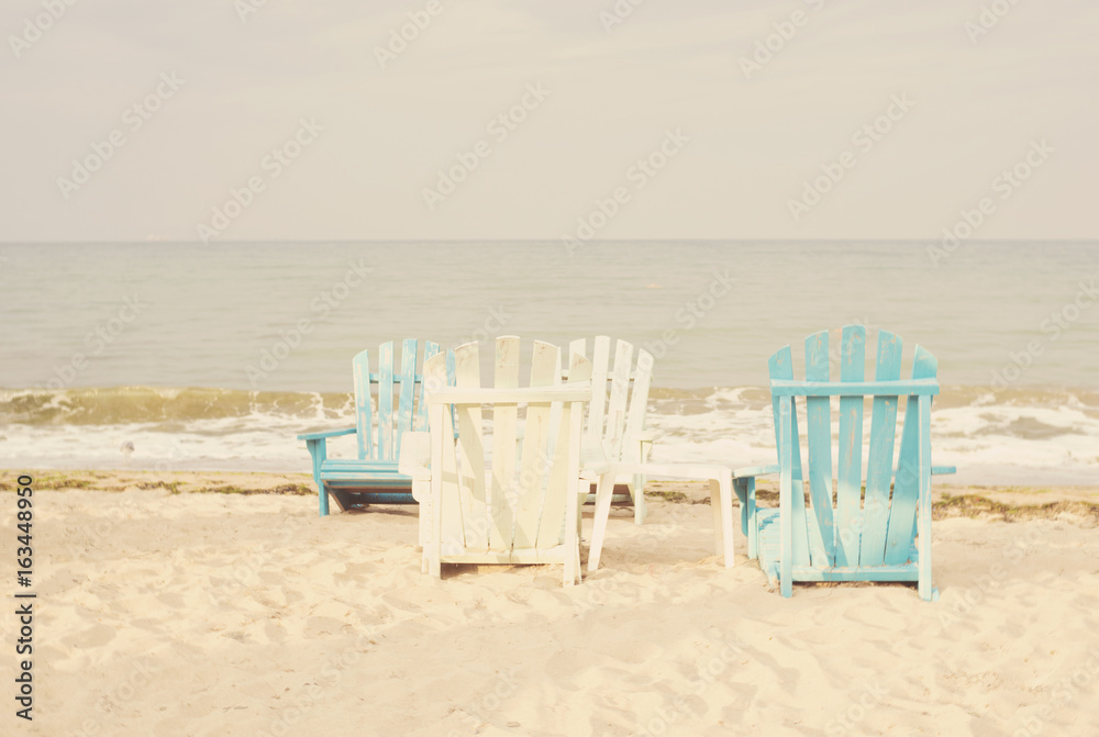White and blue beach chairs on sand seascape and bright sky in summer vacation relax. Vintage filter tinting, sun haze, glare