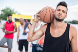 portrait of handsome basketball player with ball on shoulder standing on court