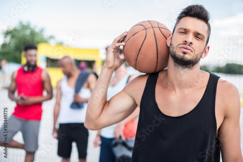 portrait of handsome basketball player with ball on shoulder standing on court