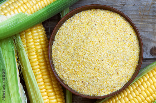 Organic maize flour in wooden bowl with fresh corn. Top view  photo