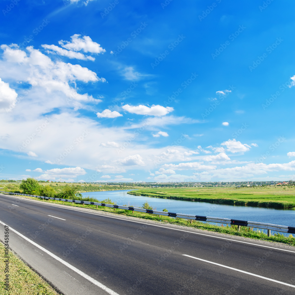 asphalt road and river along it with blue sky over