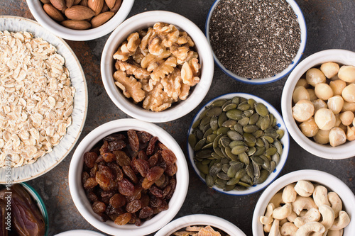 Ingredients for homemade paleo granola, different nuts and raisins, dates, seed on the grey stone background, top view