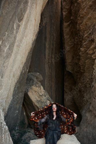 Glamour oriental woman with colorfull shawl on her head standing next to a rock