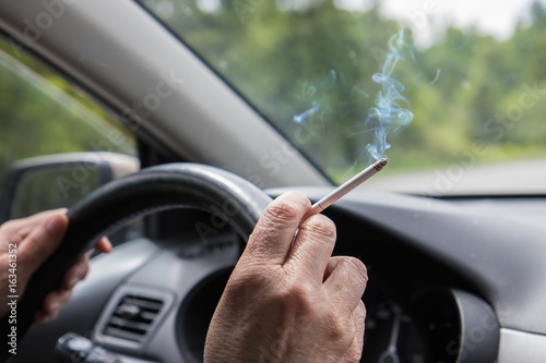 Bild auf Leinwand Smoking cigarette in the hand of elderly woman at steering wheel