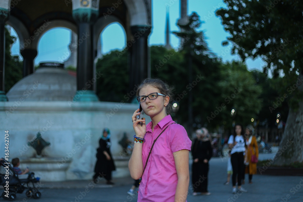 A young girl standing on the street, in the park, using a mobile phone, a story, a smile on her face, modern technology