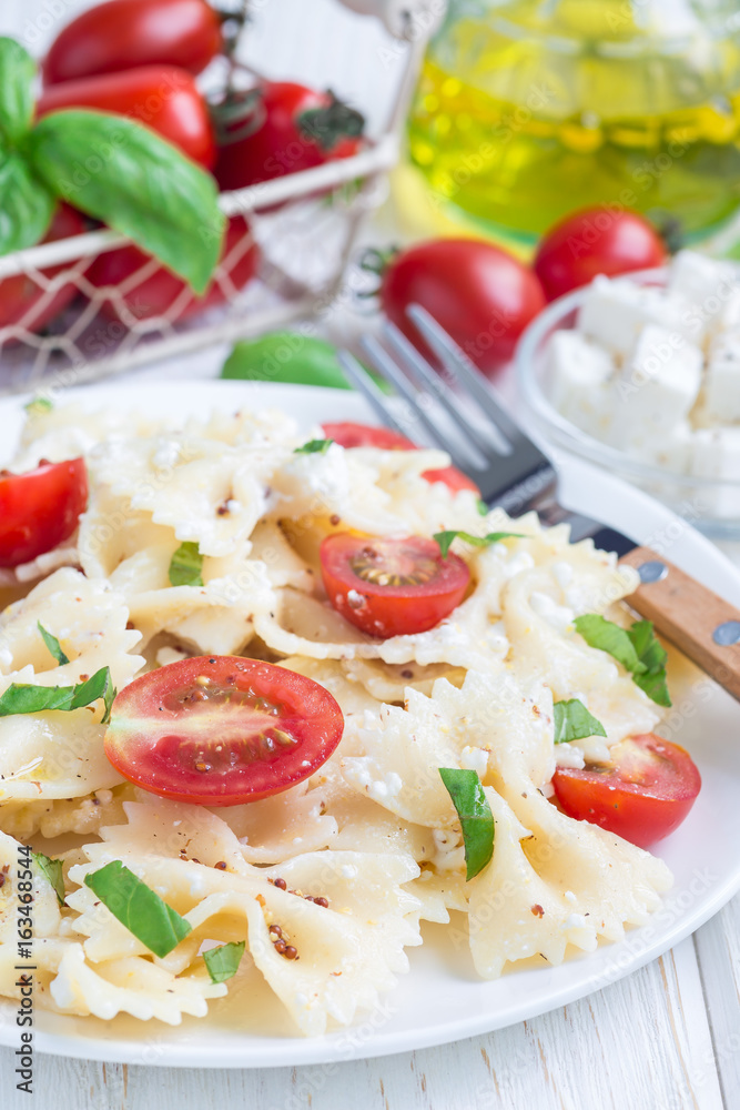 Pasta salad with tie pasta, feta cheese, tomatoes, mustard and basil, vertical