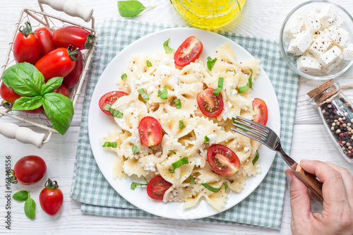 Eating pasta salad with tie pasta, feta cheese, tomatoes, mustard and basil, top view, horizontal