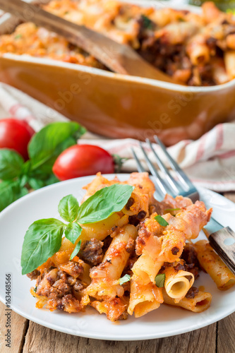 Ziti bolognese on white plate, pasta casserole with minced meat, tomato sauce and cheese, vertical