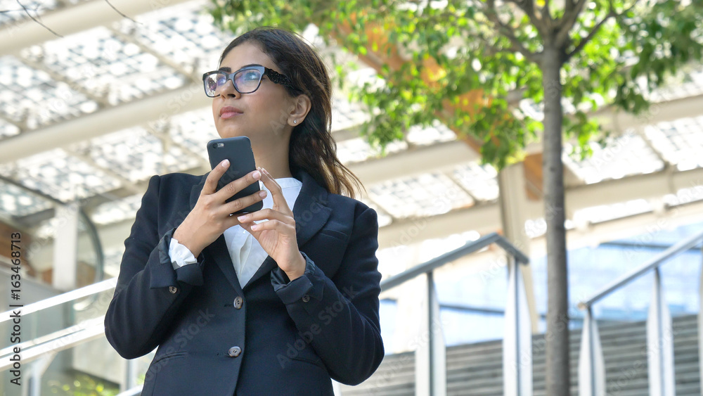 Young beautiful business woman (student) in a suit, smiling, happy, going down stairs, steps, talking on the phone, writing a message. Concept: new business, communication, Arab, banker, glasses, call Young beautiful business woman (student) in a suit, smiling, happy, going down stairs, steps, talking on the phone, writing a message. Concept: new business, communication, Arab, banker, glasses, call