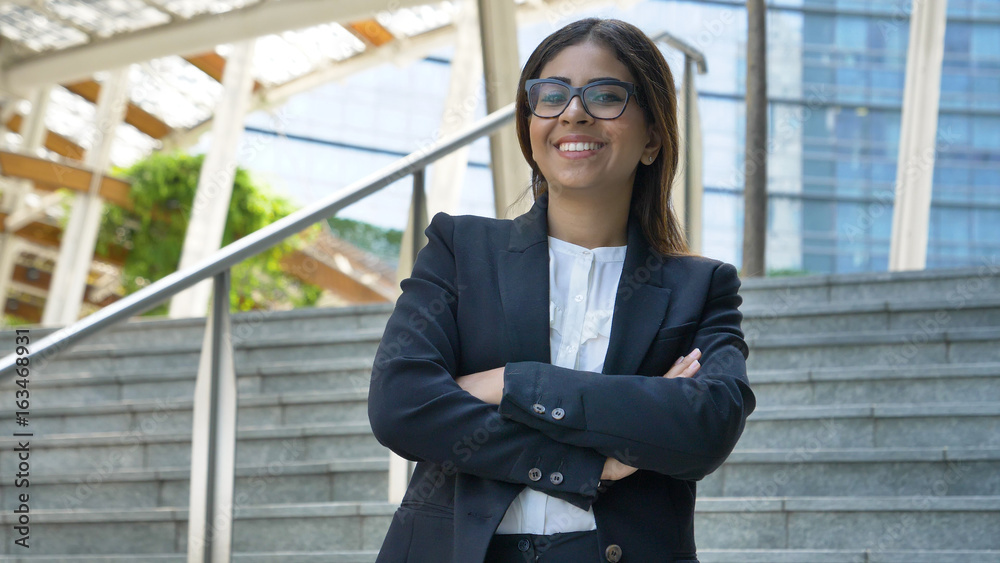 Fototapeta premium Portrait of young beautiful business woman (student) in suit, glasses, smiling, happy, walking down stairs, steps, on building background. Concept: new business, communication, Arab, banker, manager.