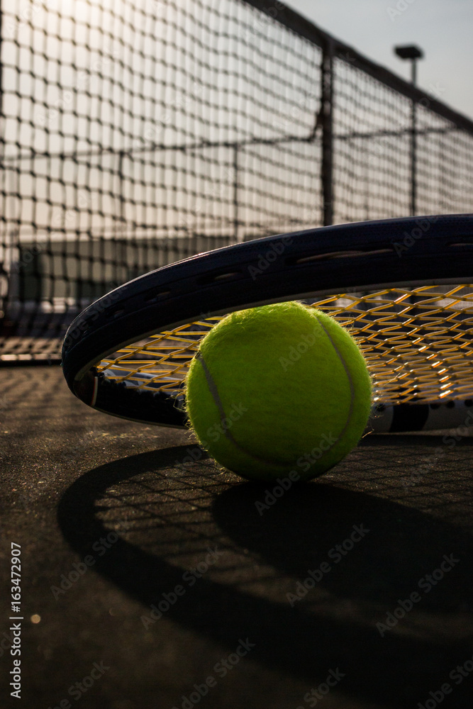 Tennis ball and racket on hard court under sun light
