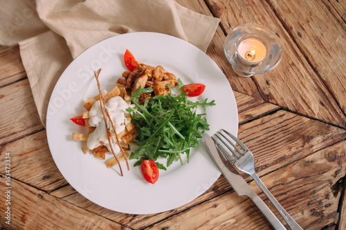 Healthy chicken salad with fresh arugula and tomato on a wooden table .