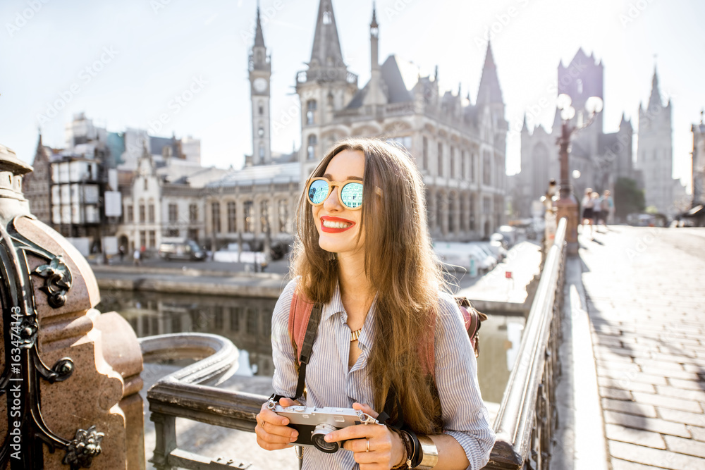 Portrait of a young woman tourist with photo camera traveling in the old town of Gent city during the sunrise in Belgium