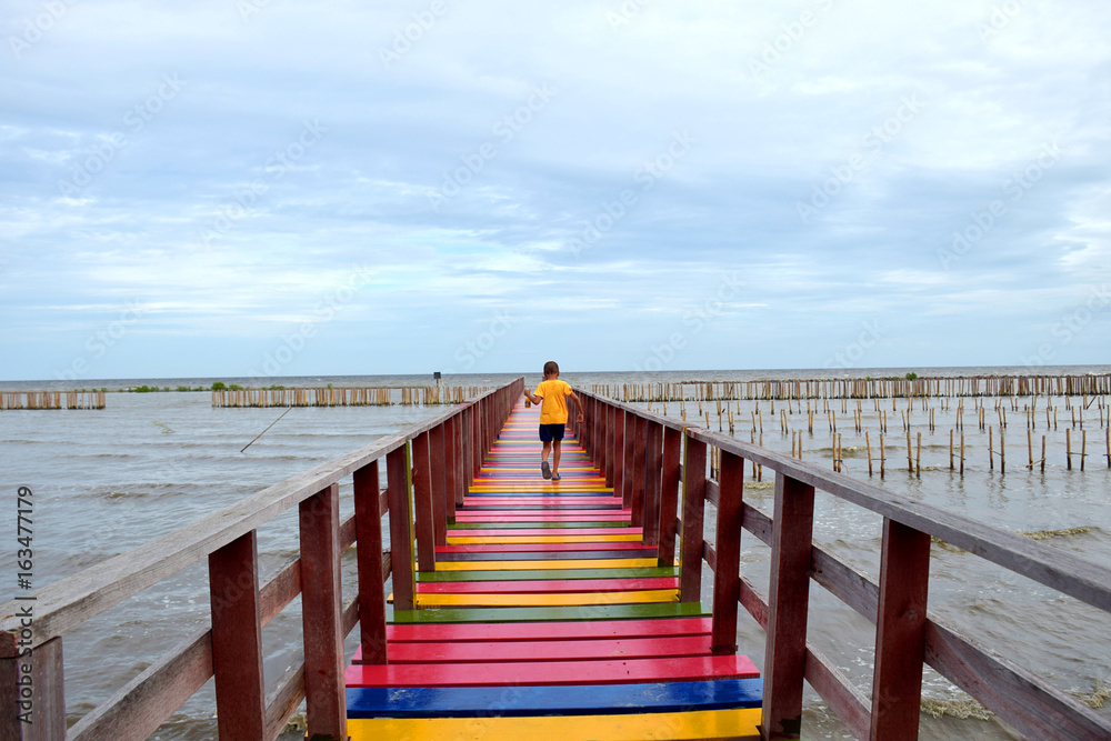 Boy walking alone sea view on a wooden bridge