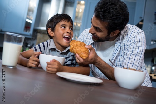 Smiling father feeding croissant to son