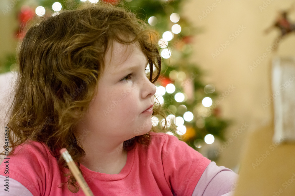 Fototapeta premium Cute little child girl writes the letter to Santa Claus near Christmas tree indoors.