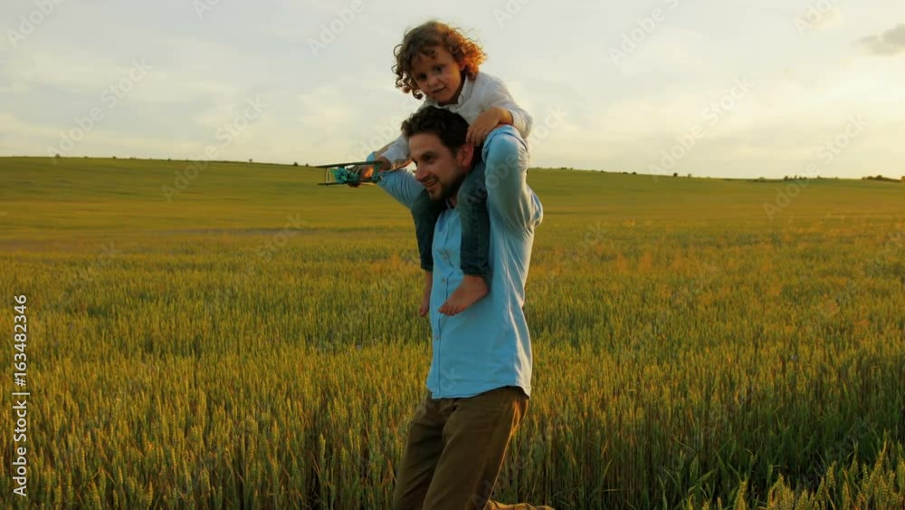 Happy father with son running in green wheat field. Young father holding his son on the shoulders. Close up Happy father with son running in green wheat field. Young father holding his son on the shoulders. Close up