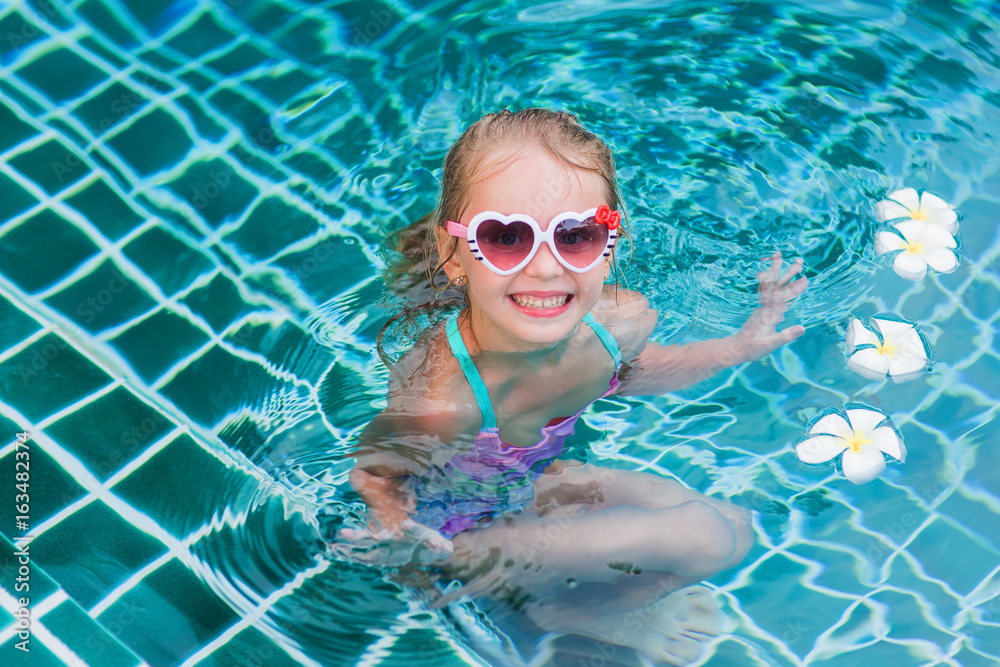 Little beautiful girl in sunglasses relaxing in the resort pool