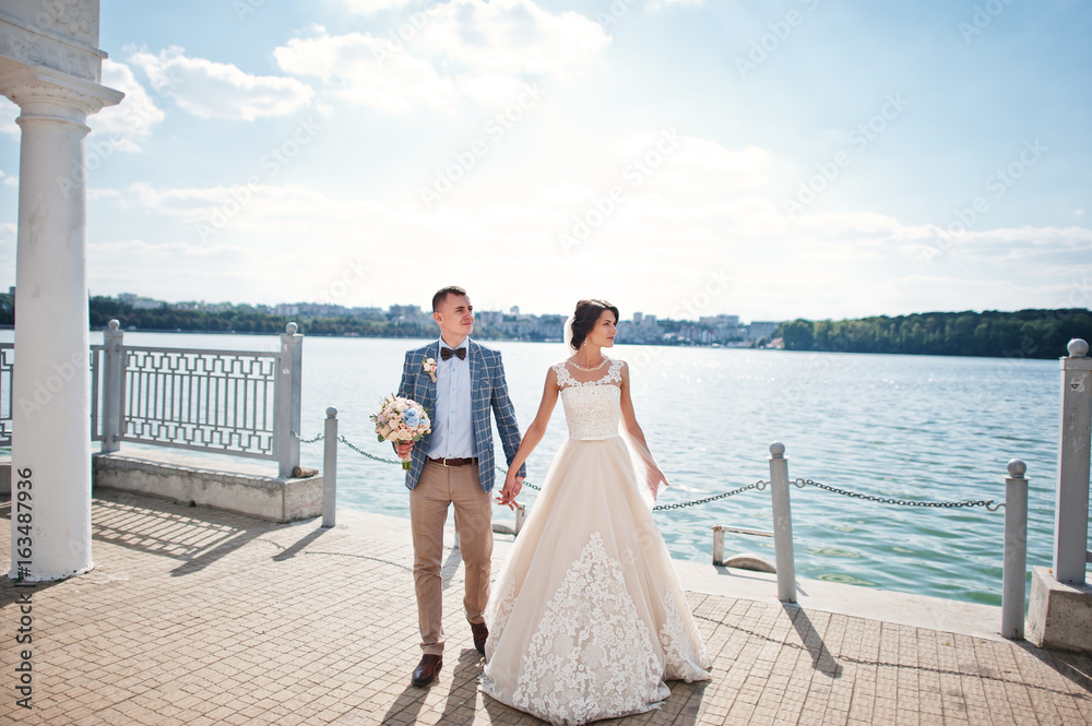 Stunning wedding couple walking on lakeside on a sunny day. Stunning wedding couple walking on lakeside on a sunny day.