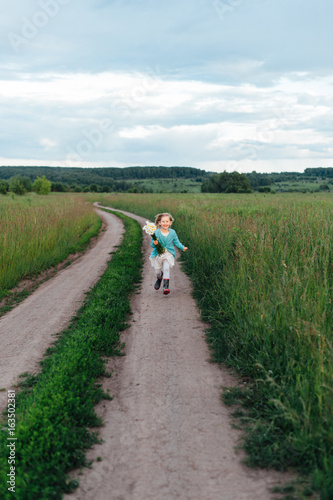 A cheerful child runs with a bouquet of daisies in boots