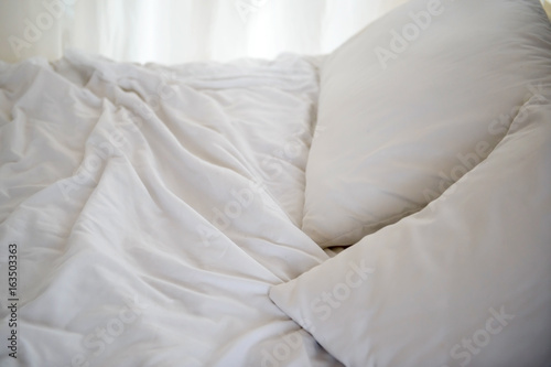 Crumpled white sheets and pillows on bed in the morning, bedroom for two people. Background white creased cloth. The texture of the fabric after sleep.