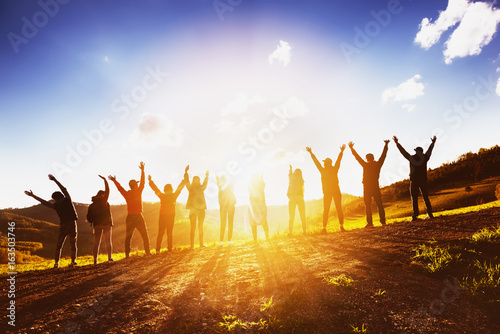 Big group of friends raising arms on sunset together