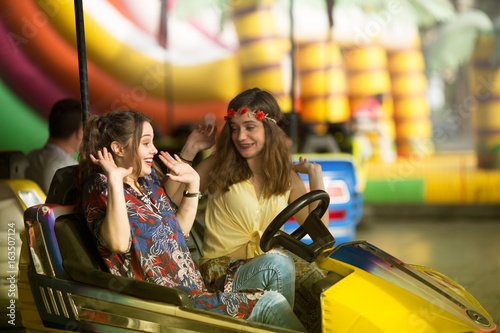 two young woman are laughing and shouting while riding a bumper car at amusement park