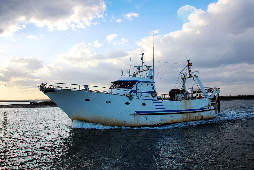 Fishing boat returning to coast at sunset with full moon Fishing boat returning to coast at sunset with full moon