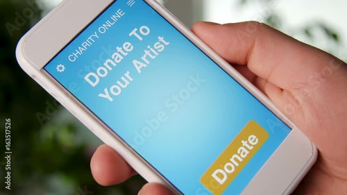 Man making an online donation to his favorive artist using charity applicaiton on smartphone photo