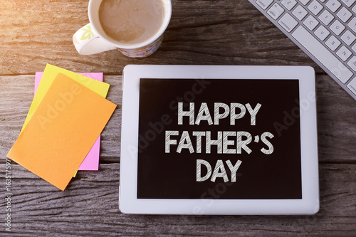 Tablet pc with HAPPY FATHERS DAY and a cup of coffee on wooden background.