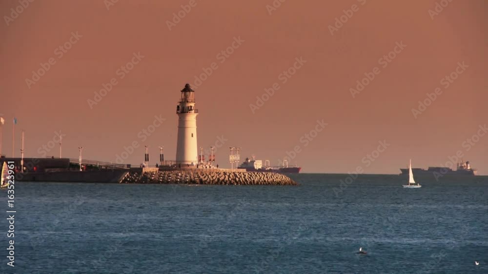 Sailboat sailing in sea,relying on lighthouse dam at dusk.water surface. Sailboat sailing in sea,relying on lighthouse dam at dusk.water surface.