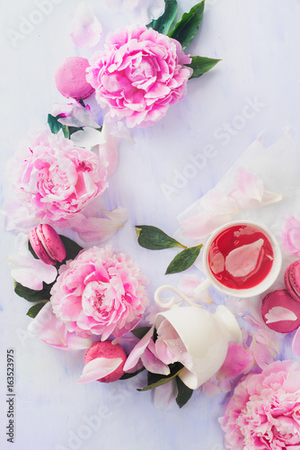 Flatlay with white coffee cup, macaroons and spilled pink peony flowers and petals
