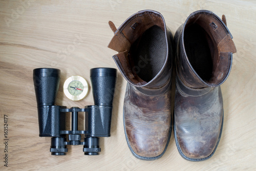 Binoculars, old boots and compass, traveler's things, on the wooden background