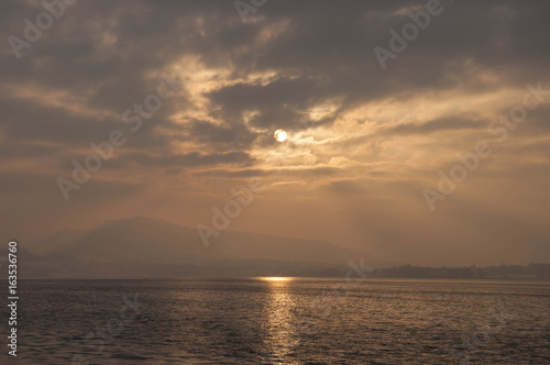 Sunset over a Swiss lake with the sun shining through light overcast.